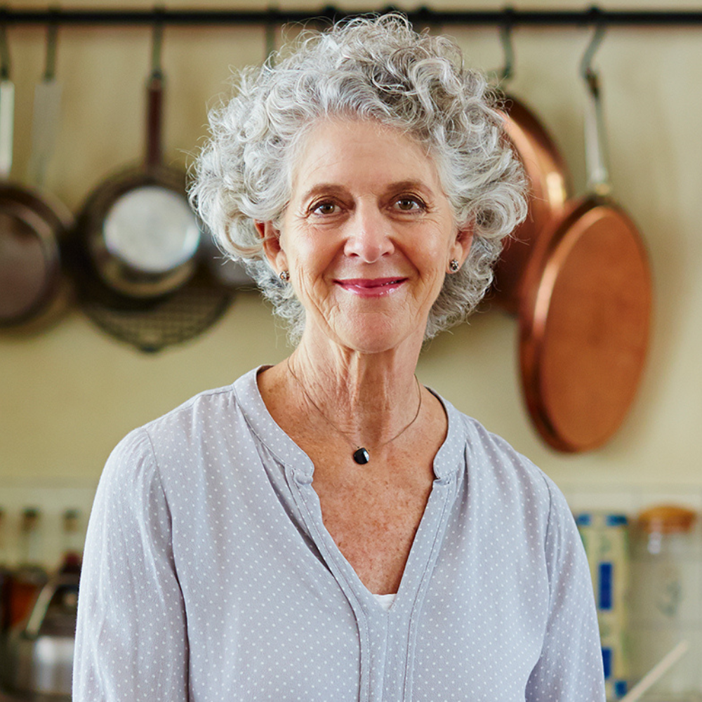 A woman standing in a kitchen. Behind her are pots and pans.