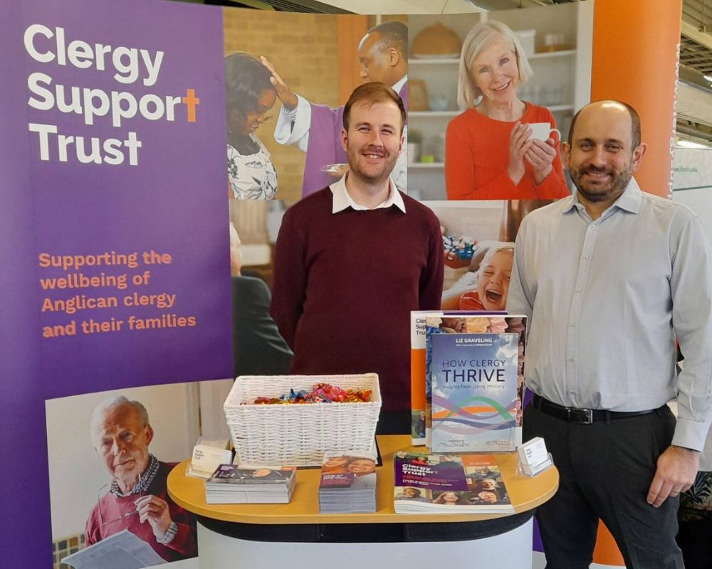 George and Nick standing in front of an orange and purple Clergy Support Trust banner.