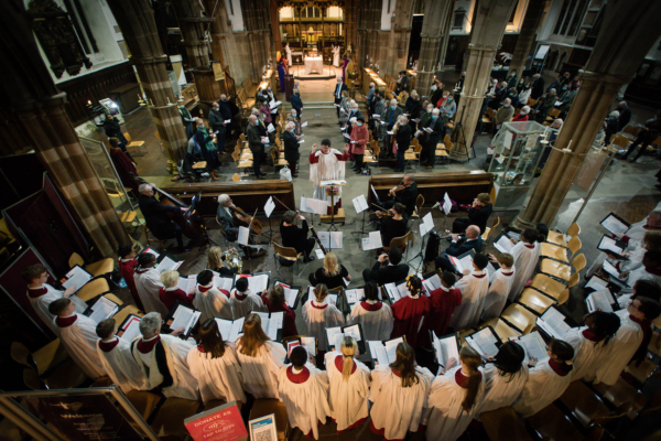 The choir performing in a darkened church, accompanied by musicians.