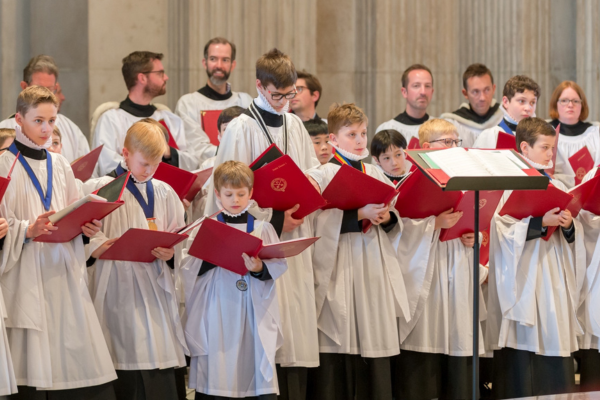 A group of young singers, dressed in white and holding red song books, prepare to perform.