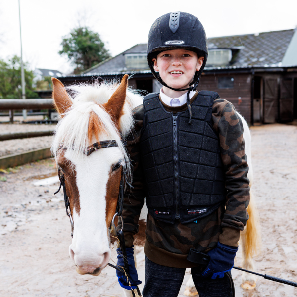 Josiah is wearing a black helmet and safety vest. He is standing alongside a white and ginger horse, Arthur.