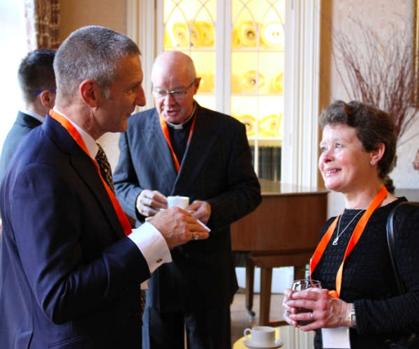 Two people, dressed formally and with orange lanyards, enjoying a cup of tea.