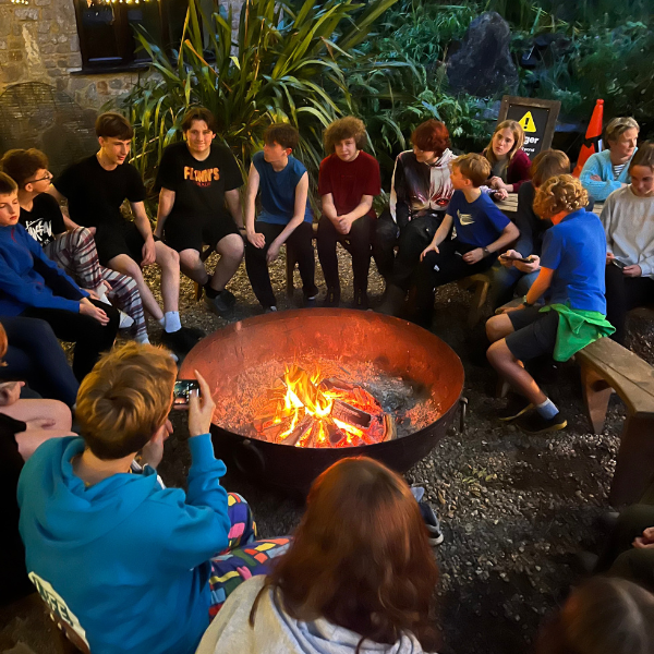 A group of young people sitting around a campfire.
