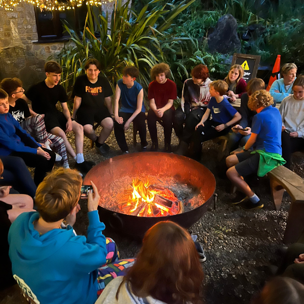 A group of young people, sitting around a campfire.