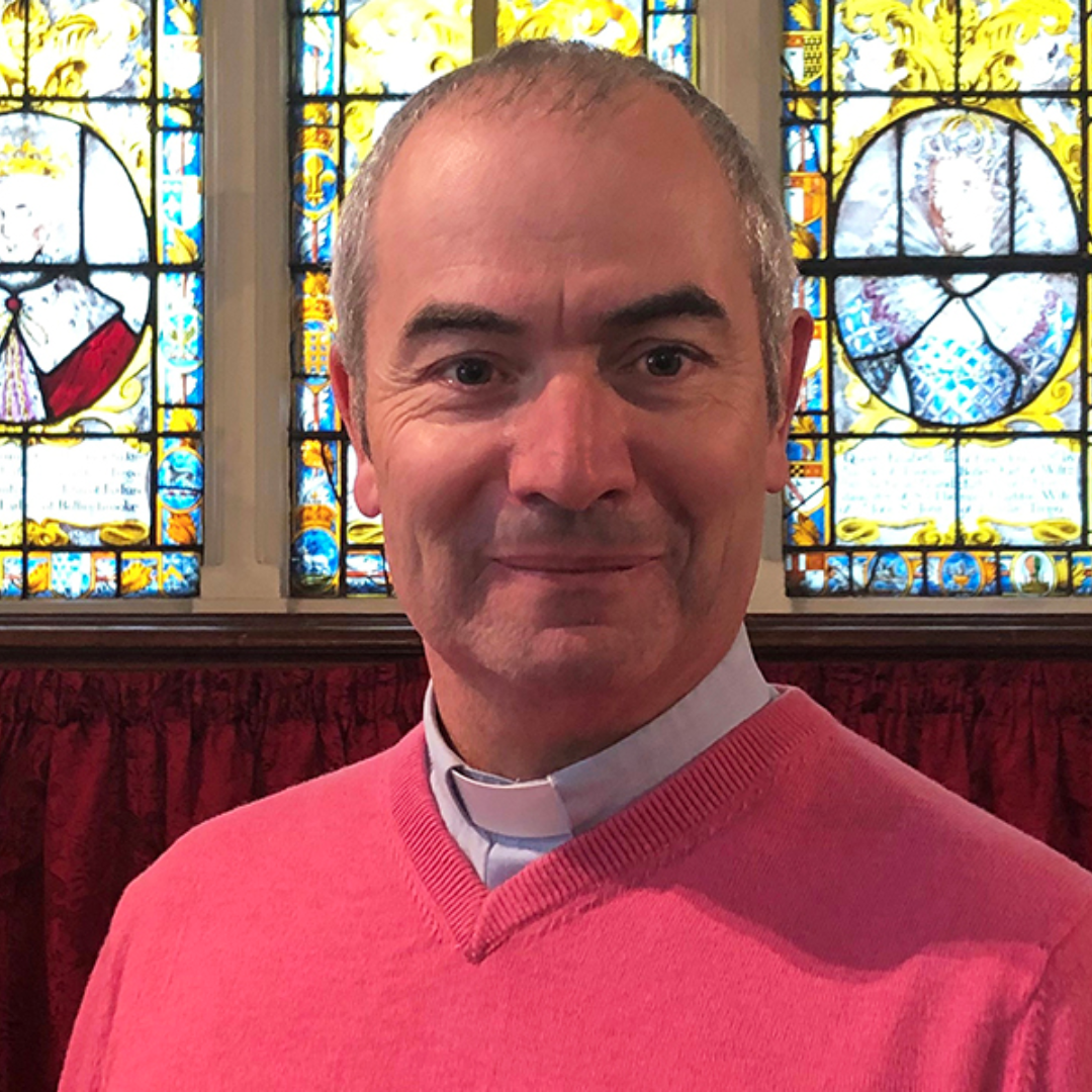 The Revd Canon Simon Butler, standing in front of a stained glass window.