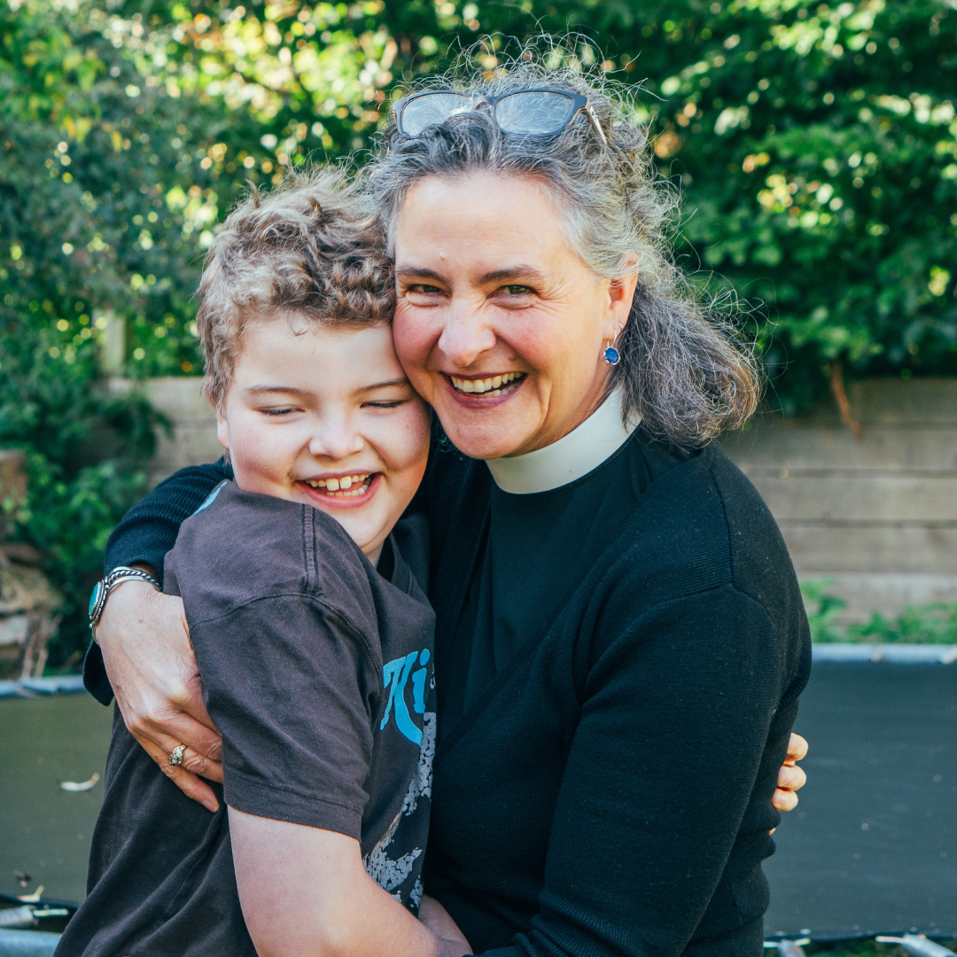 A woman holding her son, outside in the garden.