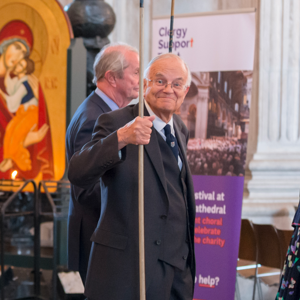 A processing Steward, looking towards the camera and smiling. He is wearing a formal black suit. A Clergy Support Trust banner is behind him.