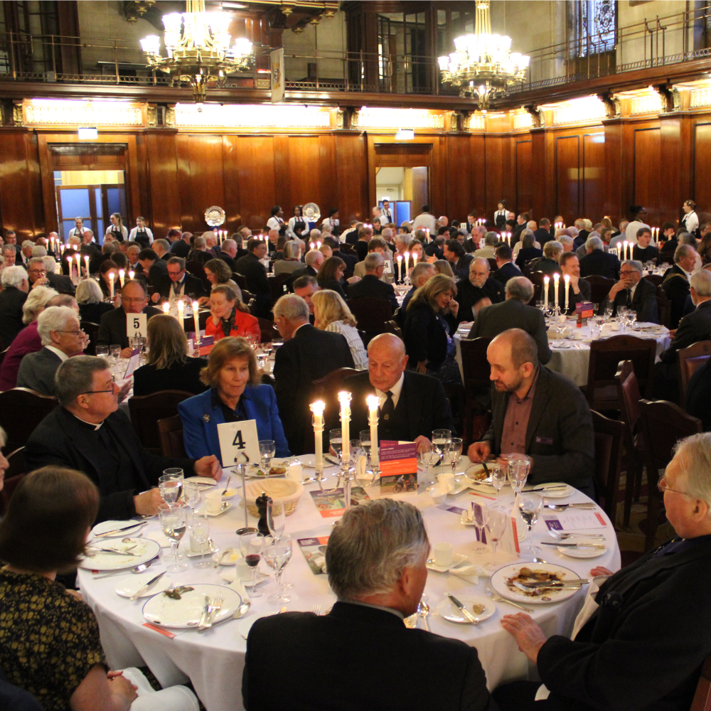 A number of circular tables, lit by candles, with guests sat around them in formal dress.