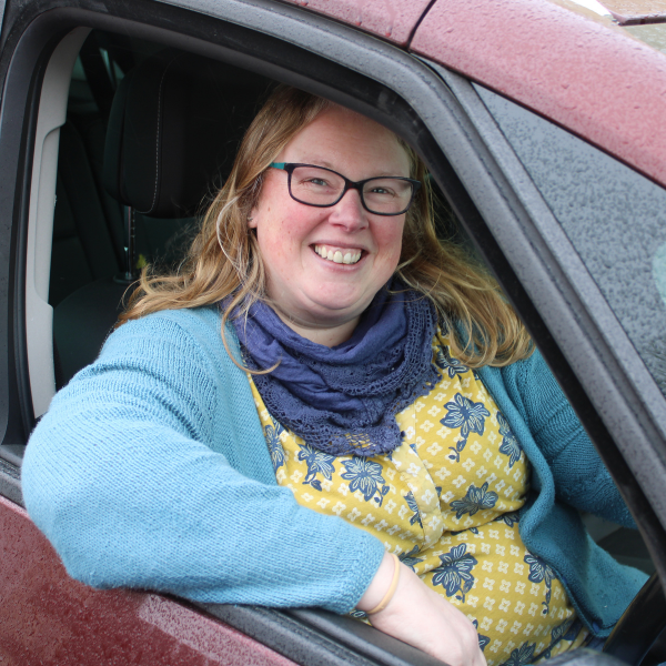 Becca, wearing a light blue cardigan, sat inside a red car, with the window open.