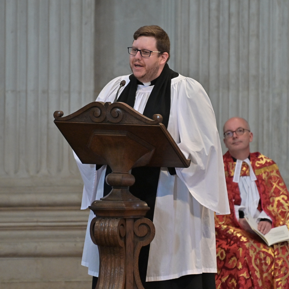 The Revd Michael Edwards is dressed in a white robe, addressing the congregation from a wooden lectern.