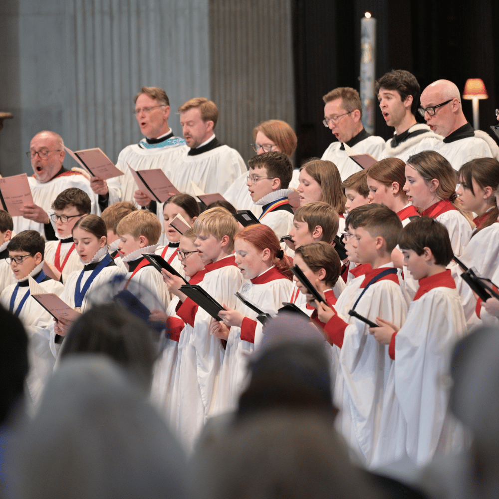 A choir, dressed in white and red robes, singing from their hymn sheets.