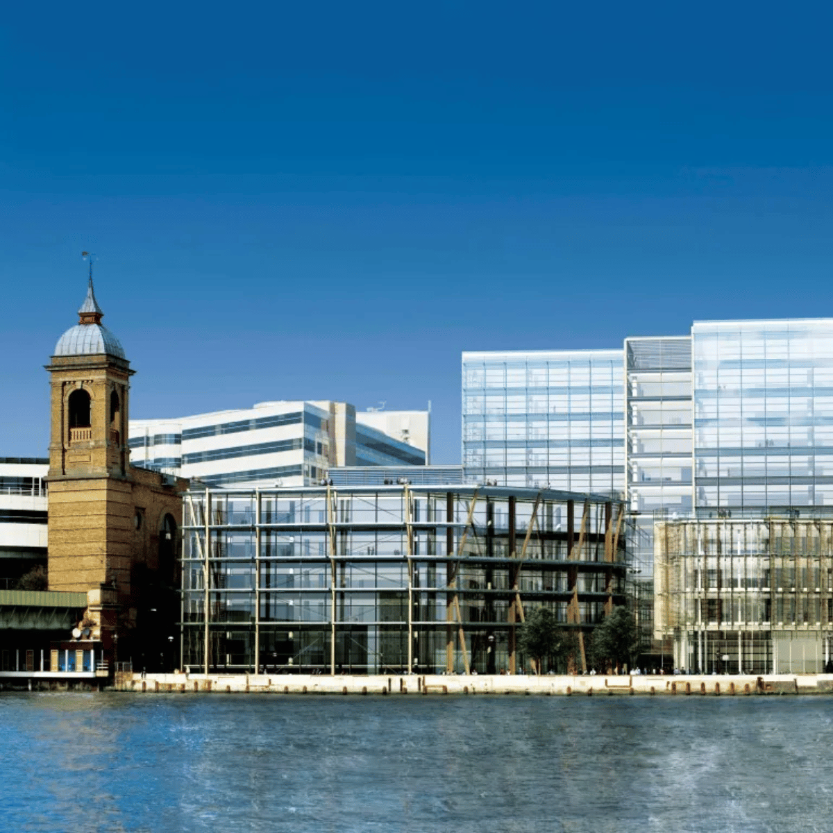The exterior of 1 Angel Lane, a glass building sat snug against the blue of the River Thames on a sunny day.