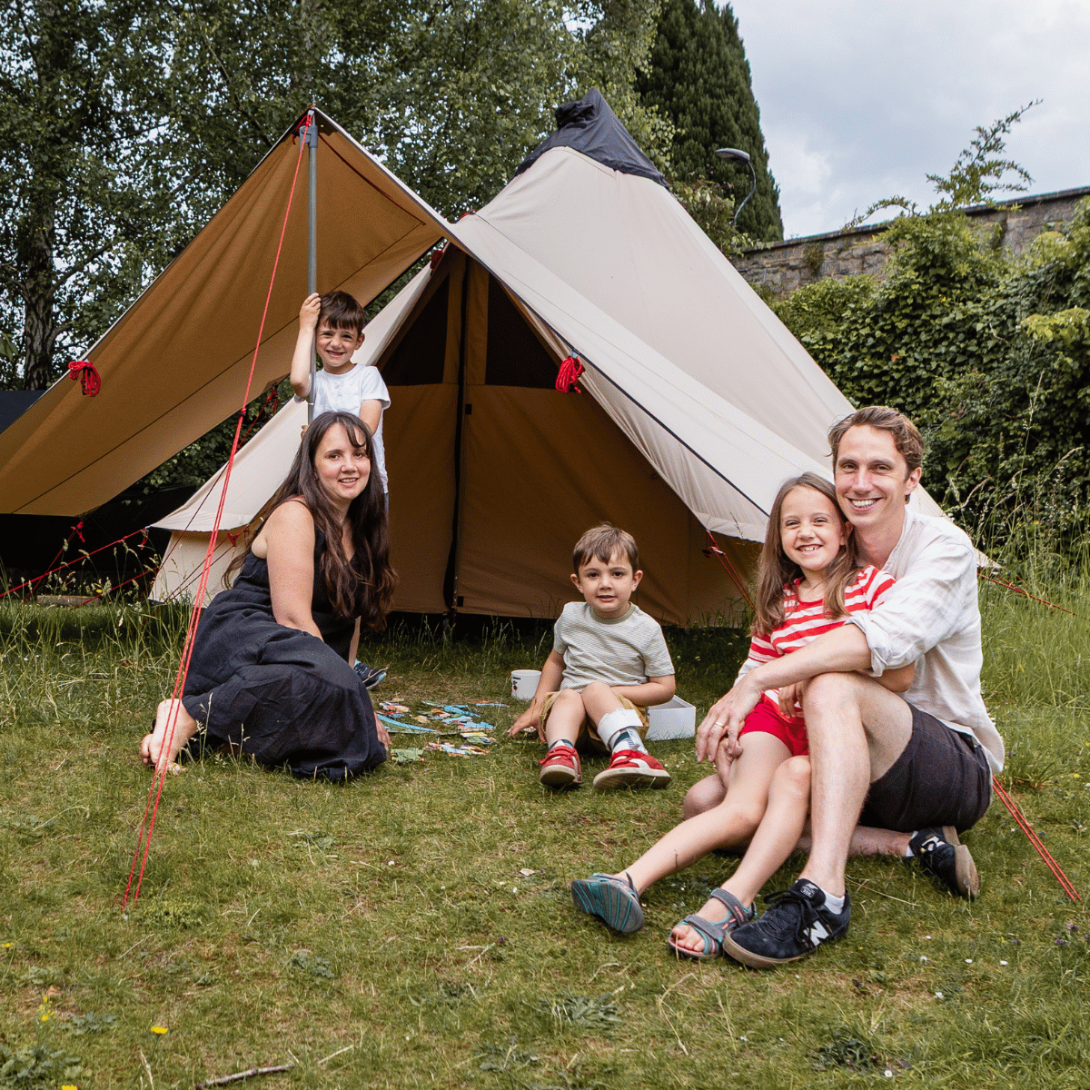 Esther, Matt and their children are playing in the garden, beneath a beige cloth tent on a cloudy day.