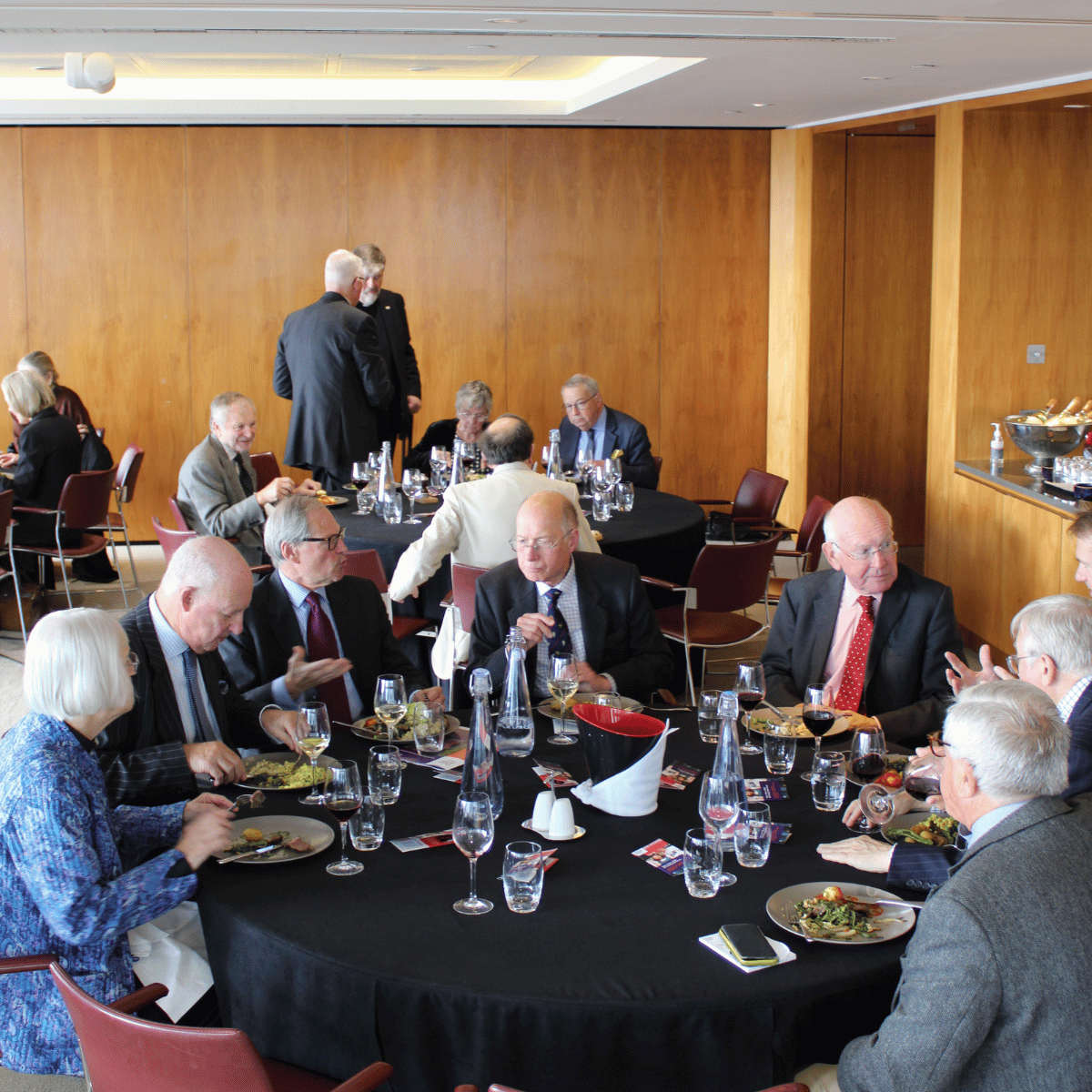 A group of formally dressed Governors are sat at a circular table, enjoying a meal and deep in conversation.