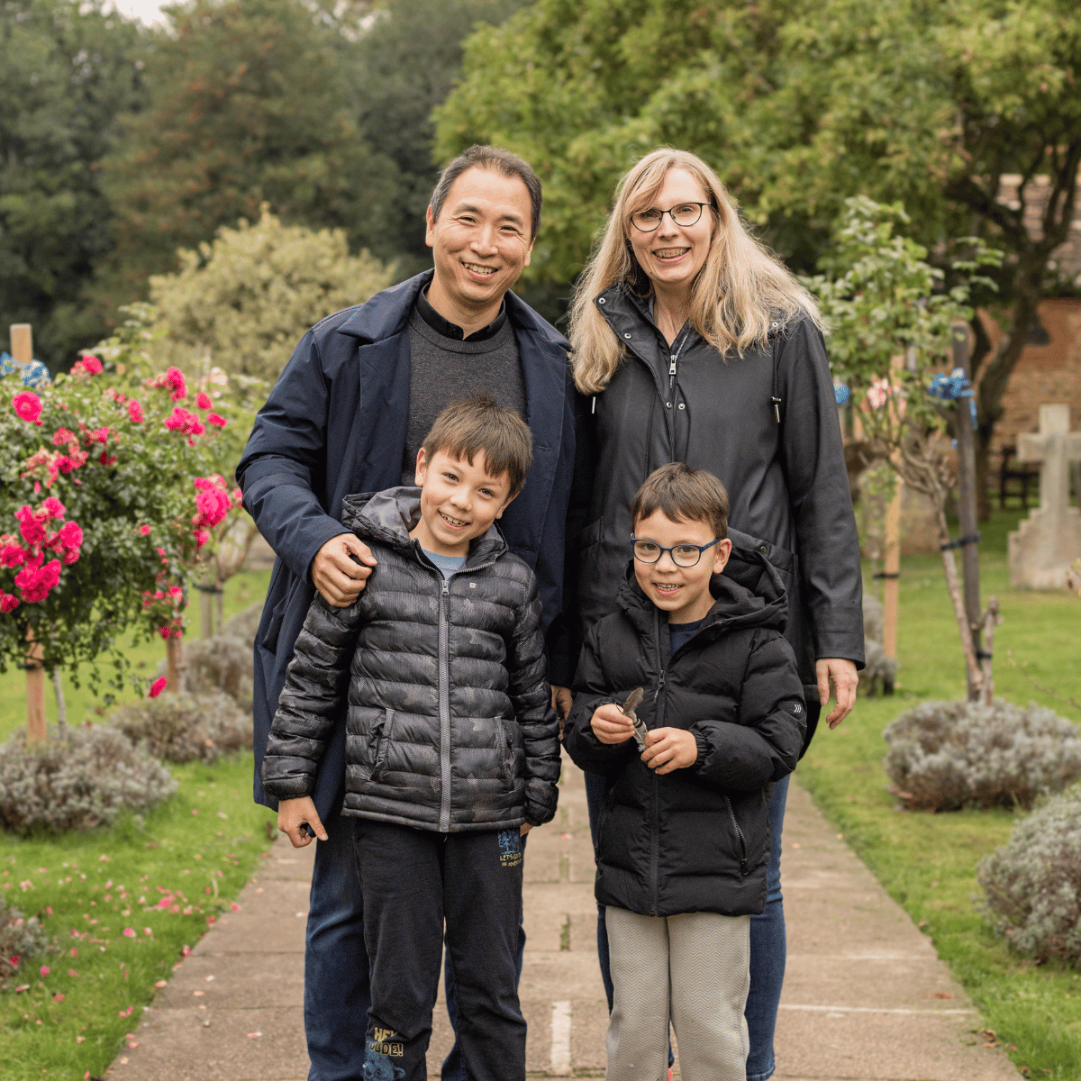 Jun, his wife and sons are stood together, dressed in their winter coats, on a footpath with grass and trees.