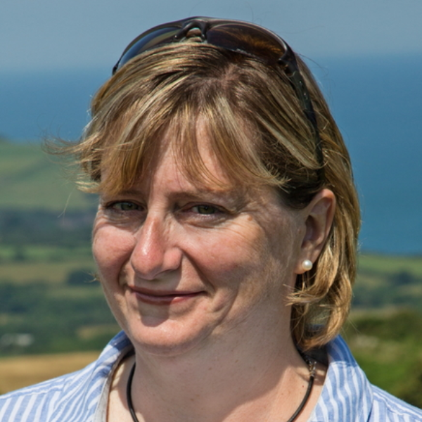 Patience is wearing a blue and white stripped shirt. A countryside scene of the sea is in the background.