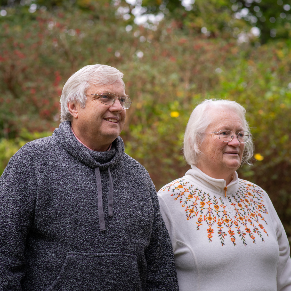 Paul is dressed in a grey hoodie, while Jo is wearing a white jumper. They are stood in their local park, looking off into the distance.