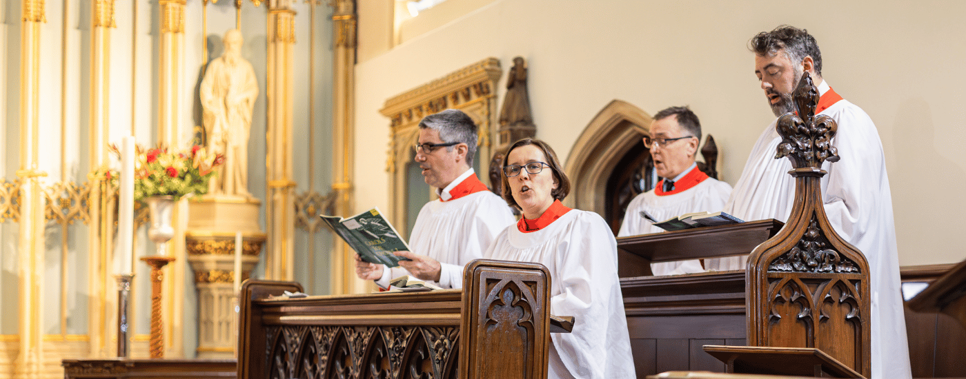 Four choristers, dressed in white and red robes, are singing from their pews.