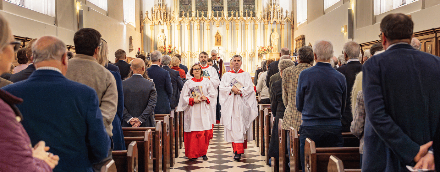 Four choristers, dressed in white and red robes, are walking down the aisle of the Church.