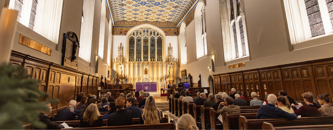 The interior of The King's Chapel of The Savoy. Guests are sat at pews, waiting for the service to begin.