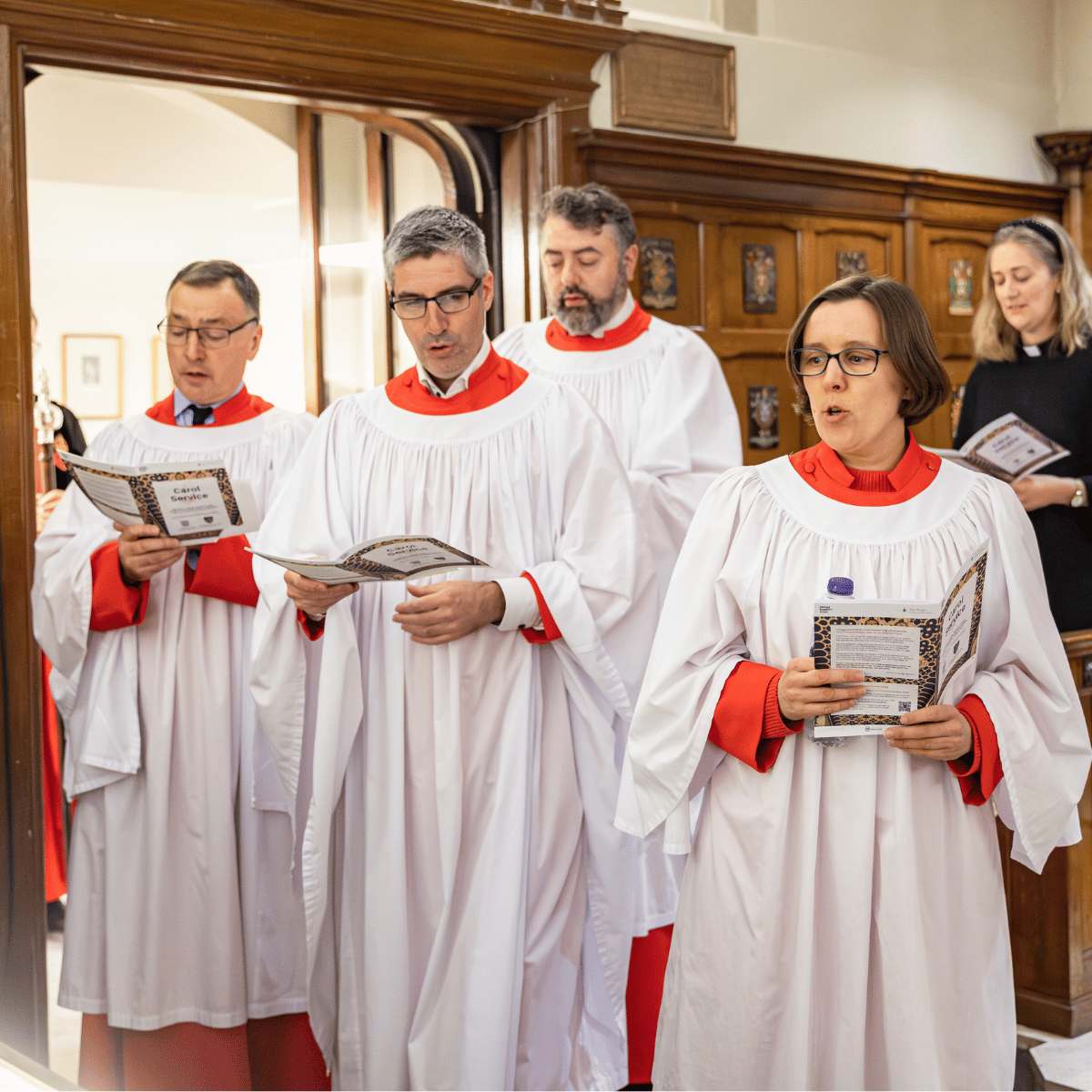 Choristers are dressed in white and red robes, singing from the Order of Service.
