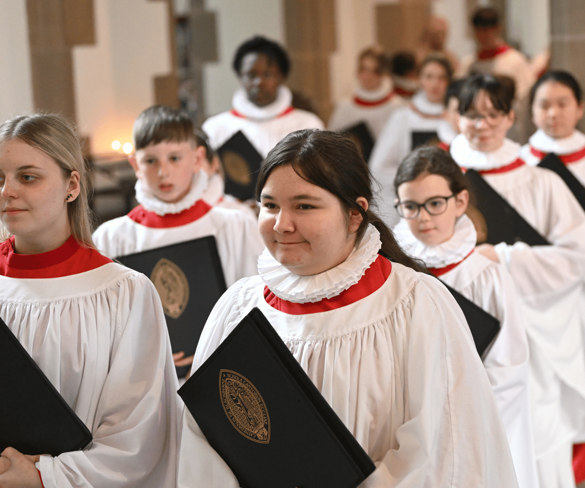 Choristers in white robes are walking in lines of two inside a Church.