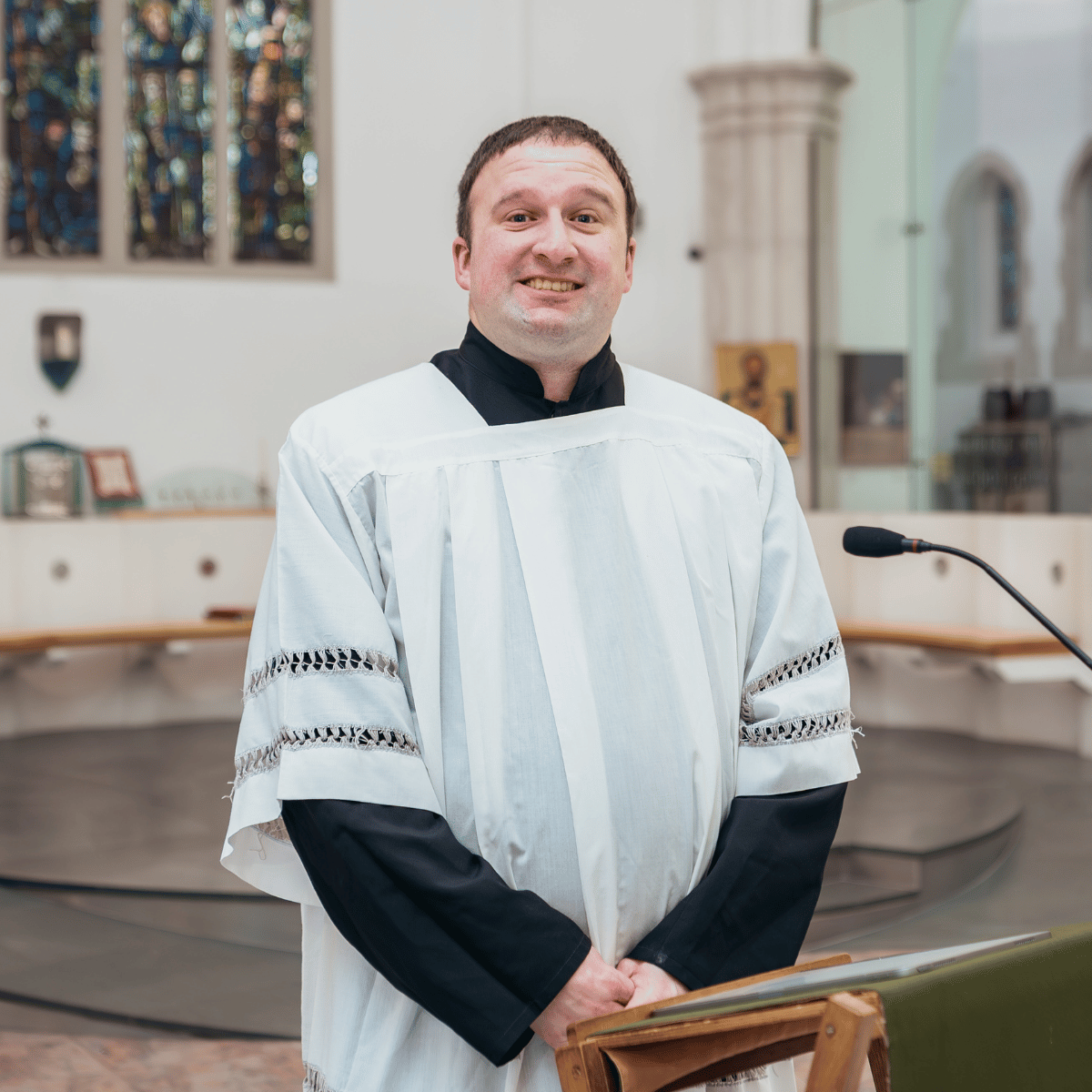 Ben is wearing a white robe, and is standing behind a small lectern with a microphone.