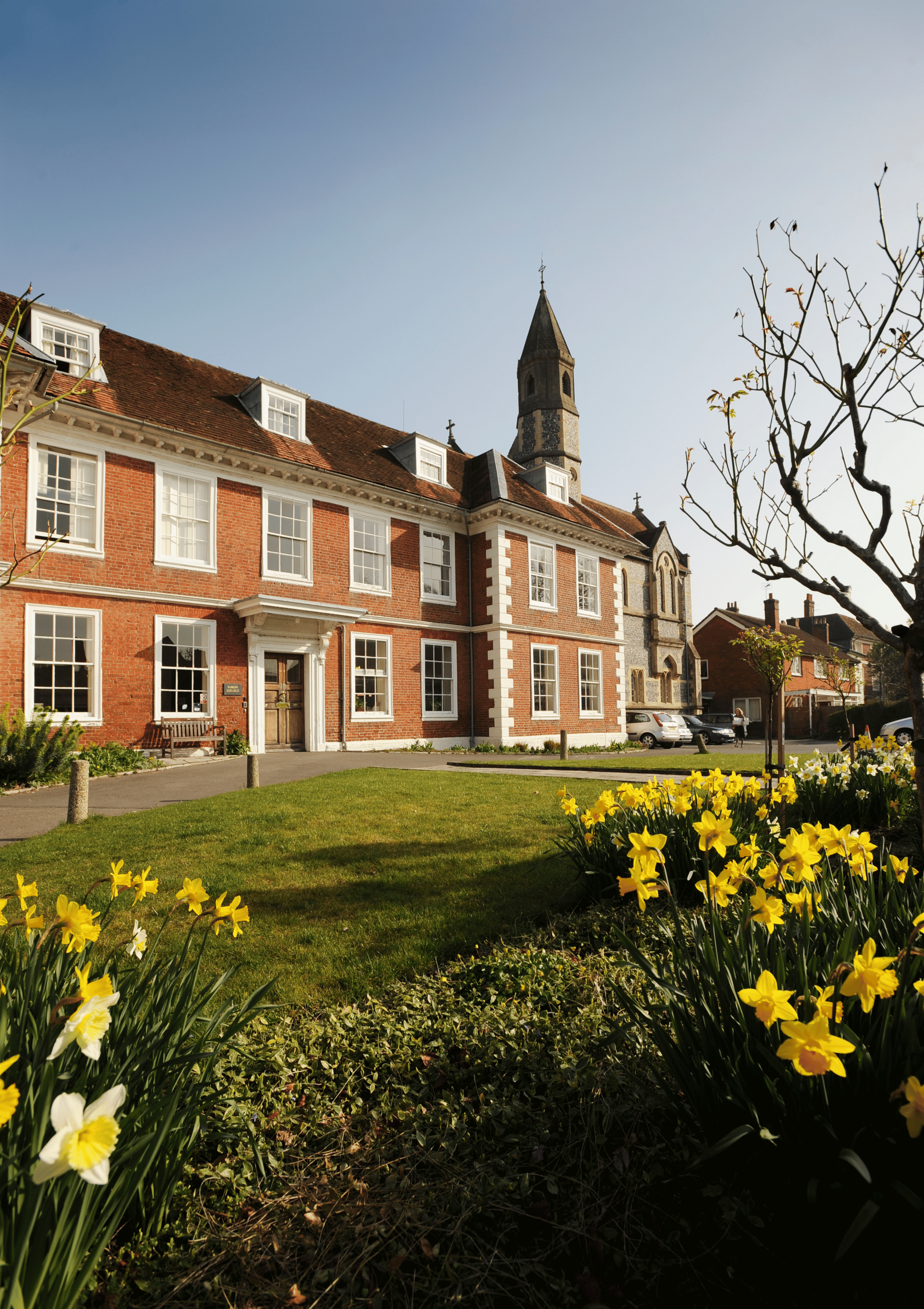 The exterior of Sarum College, a Victorian red-bricked building, with a garden of daffodils in the foreground.