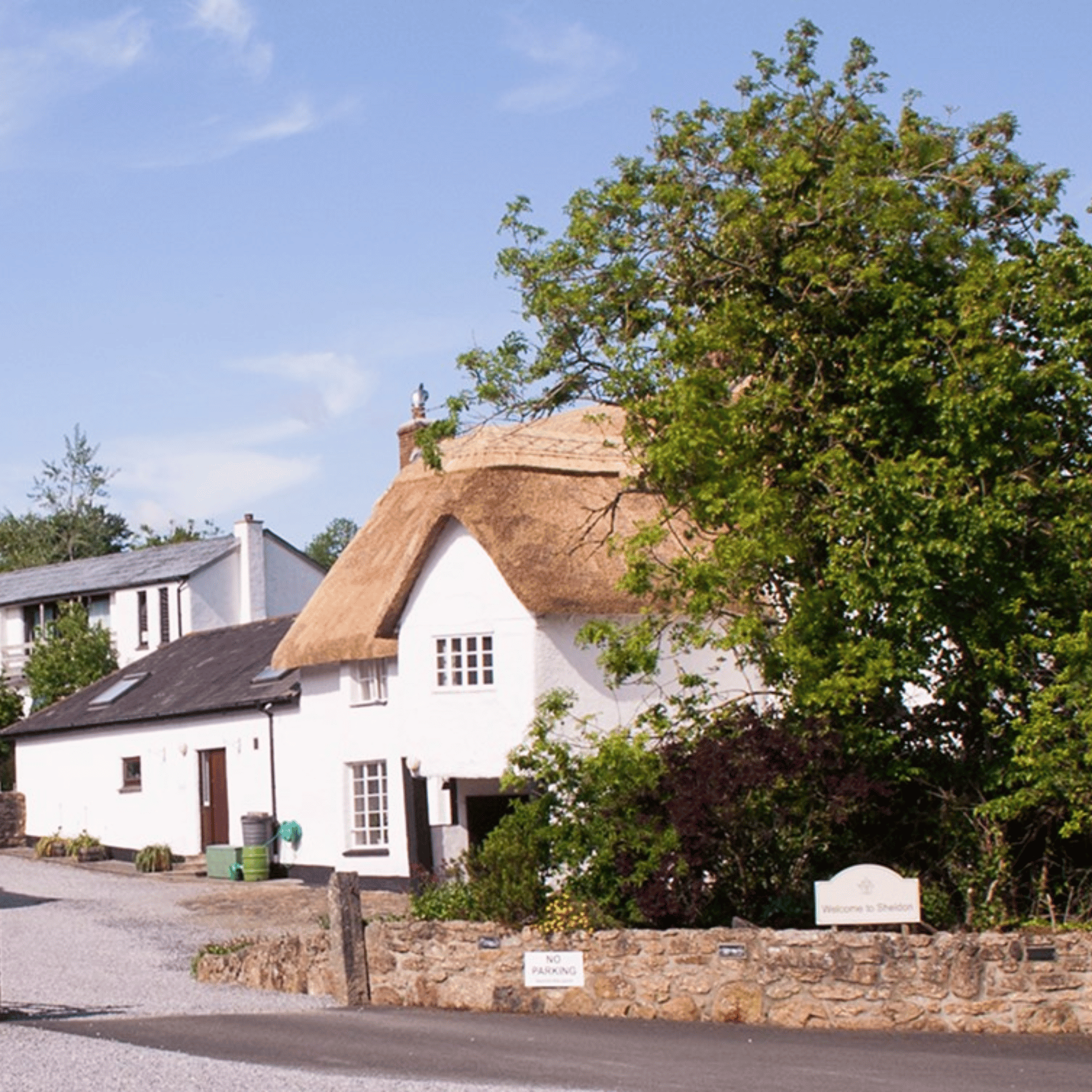 The Sheldon Retreat Centre. Beside a quiet road is a white house, with a thatched roof.