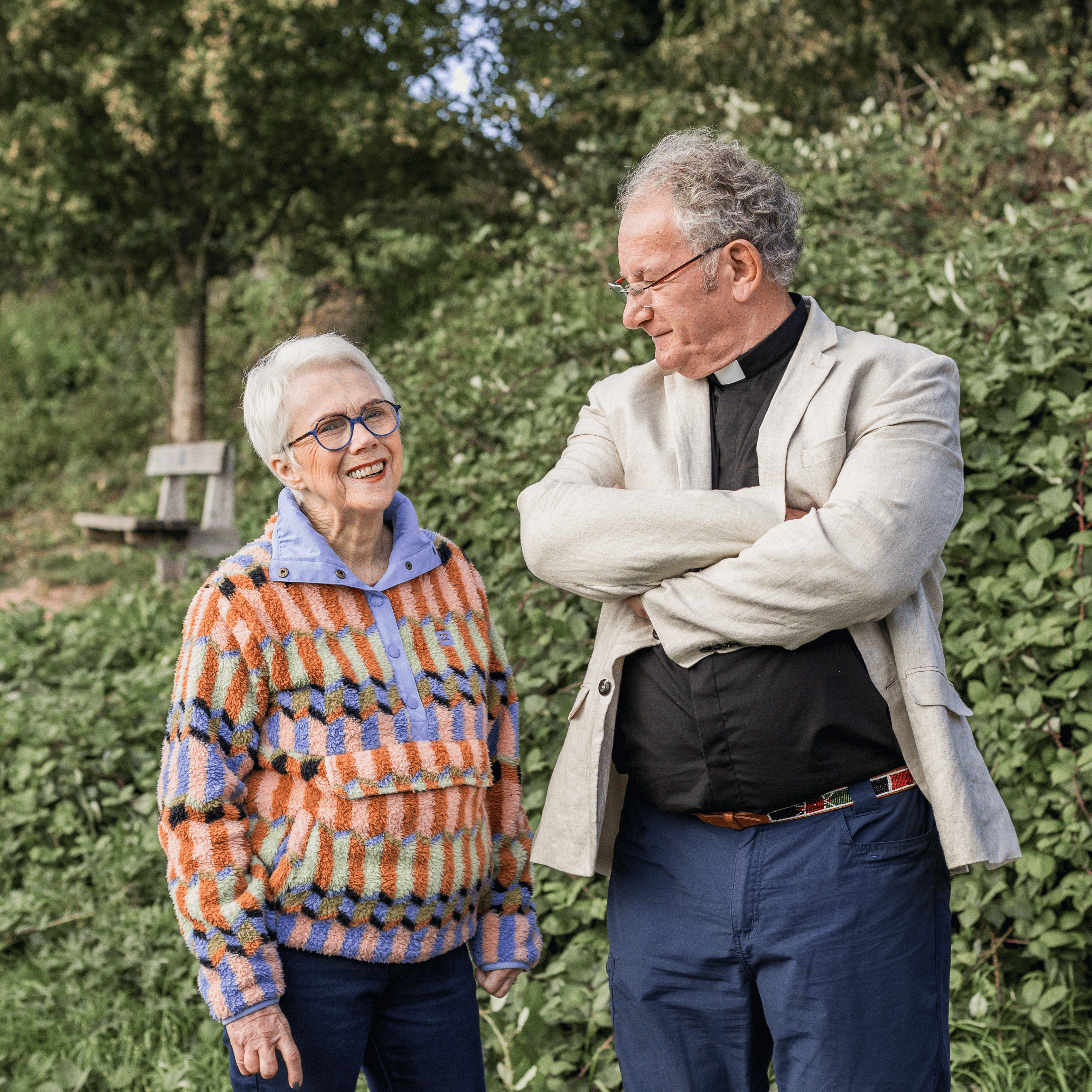 Michael is wearing a black shirt and white clerical collar. His arms are crossed, and he's looking down at Sybil. Sybil is wearing a multicoloured fleece.