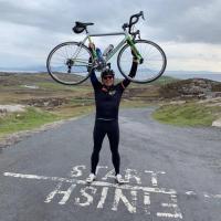 Barry, holding his bike triumphantly in the air, the road and hills behind him.