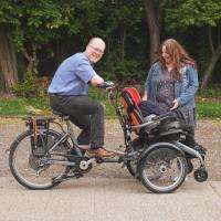 Mira with her parents, on a bicycle and wheelchair, in a park.