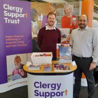 George and Nick standing in front of an orange and purple Clergy Support Trust banner.