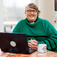 Helen, sat at a table with a laptop.