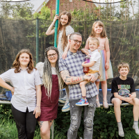 Sam and his family, looking at the camera and smiling, standing in front of a trampoline in their garden.