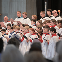 A choir, dressed in white and red robes, singing from their hymn sheets.