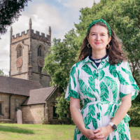 Rebecca is dressed in a green and white dress, standing in front of a church.