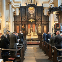 The interior of St Magnus the Martyr Church. Rows of worshippers are dressed formally, and stood in their pews, singing from the Order of Service.