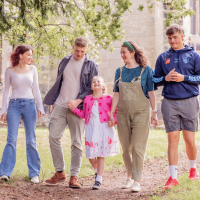 A family stood outside of a stone church and vibrant green trees.