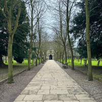 The exterior of Trinity Church, Stratford-upon-Avon. A paved pathway leads through two parallel lines of tall trees.