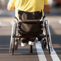 As seen from behind, a man wearing a yellow T-shirt and using a wheelchair is moving away from the camera.