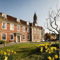 The exterior of Sarum College, a Victorian red-bricked building, with a garden of daffodils in the foreground.
